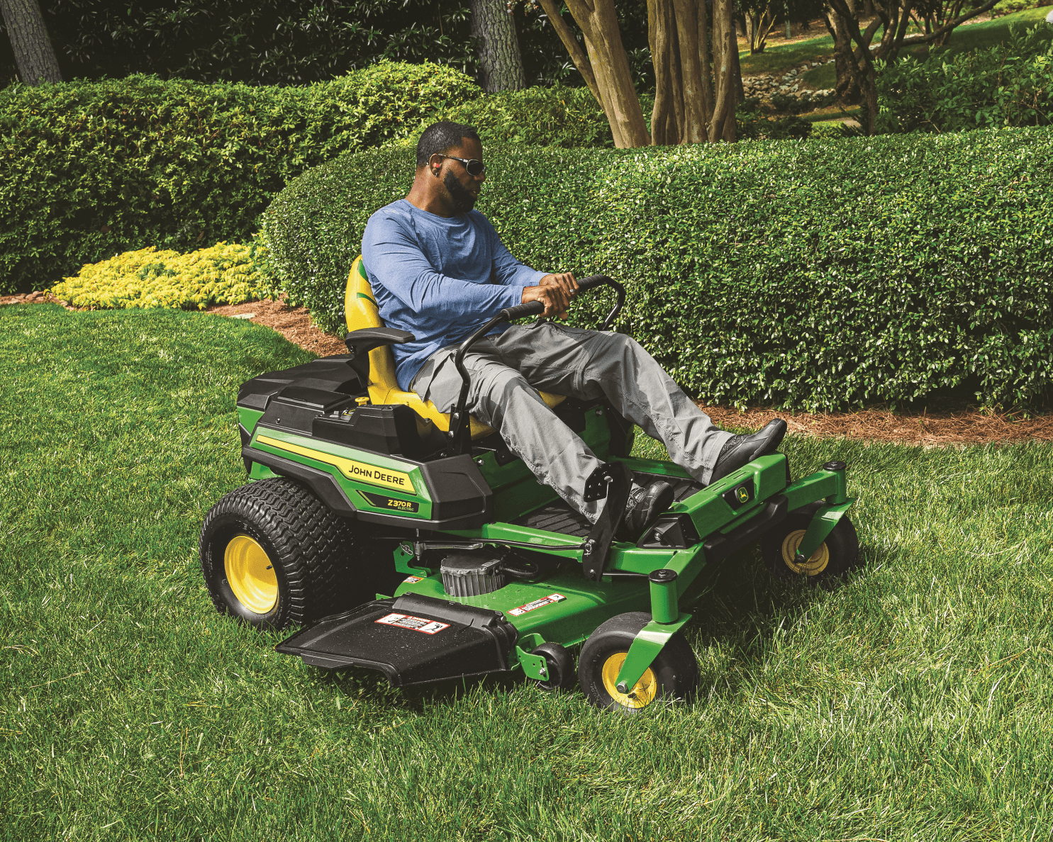 A worker on a John Deere Z370R electric zero-turn mower maintains his lawn on an urban farm in California.