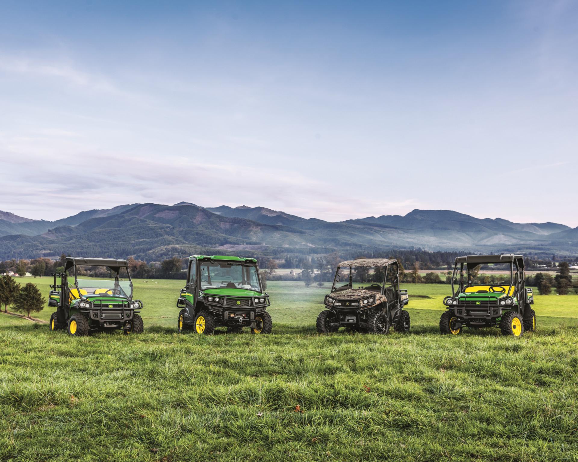 A lineup of John Deere Gators in front of a mountain range.