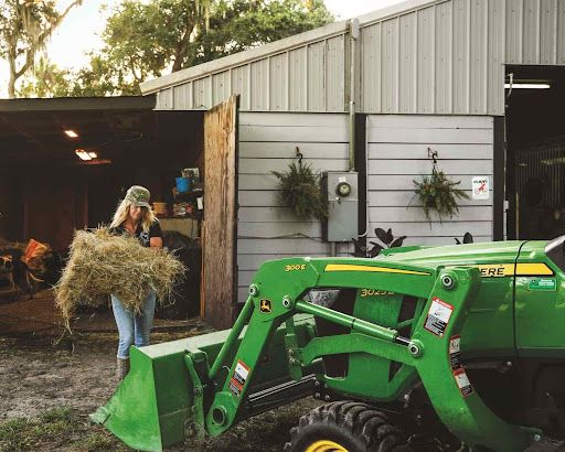 John Deere tractor with loader being loaded with a hay bail outside a barn