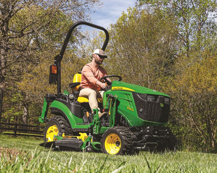 A John Deere 1025R mows grass on a property.